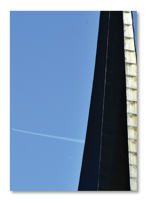 Fotografie. Minimalismus. Ausschnitt eines Kirchturms vor blauem Himmel. Im HIntergrund ist ein Flugzeug zu sehen.